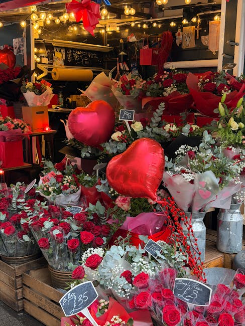 A vibrant display of fresh floral arrangements and bouquets at a florist stall, featuring predominantly red and white roses, spray carnations, and small white filler flowers. The flowers are artistica