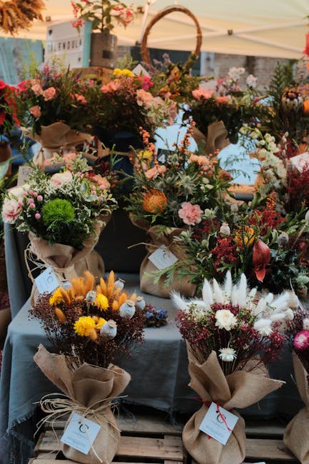 A display of various fresh flower bouquets arranged on tables at an outdoor market stall. The arrangements feature a mix of pink roses, white daisies, yellow chrysanthemums, and green foliage wrapped 